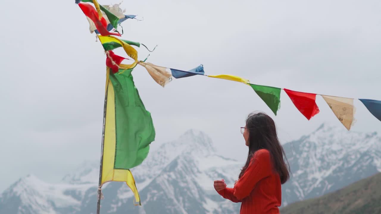 在印度拉胡尔的沙舒尔修道院，年轻的印度妇女手持经幡站在白雪覆盖的喜马拉雅山脉前。女孩看山，享受放松，宁静的气氛。视频素材