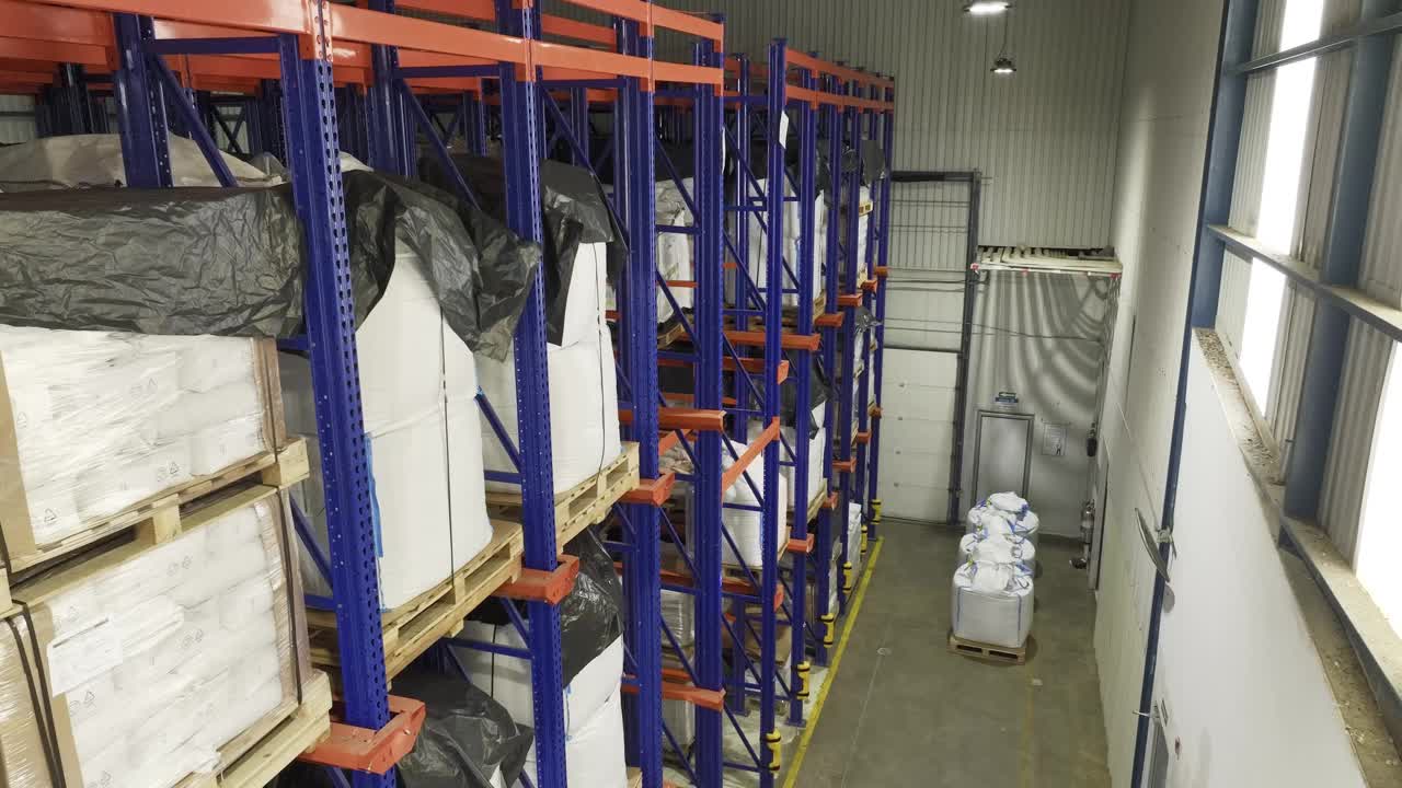 Inside a warehouse: many shelves laden with neatly stacked pallets. Camera moving from one side to another while staying up. Managing goods, storage, logistics.视频素材