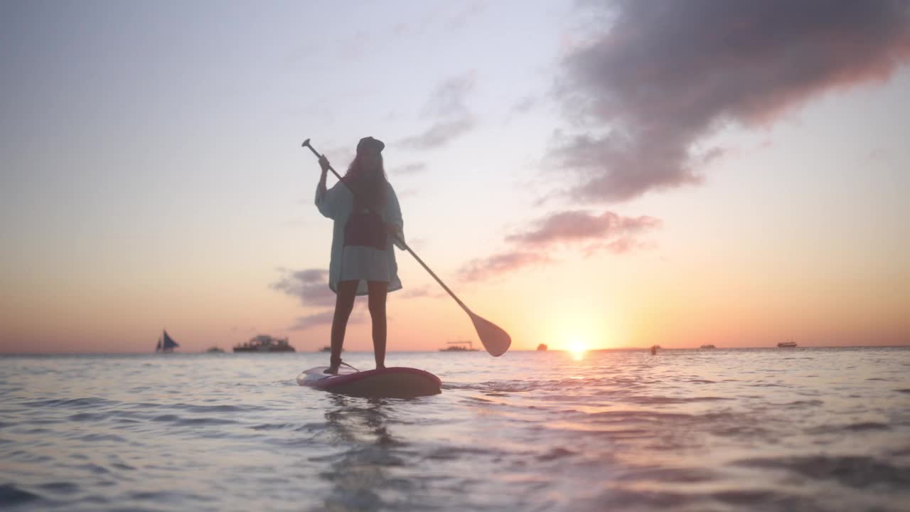 一名女子在海上的SUP板上，在美丽的日落中划桨视频素材