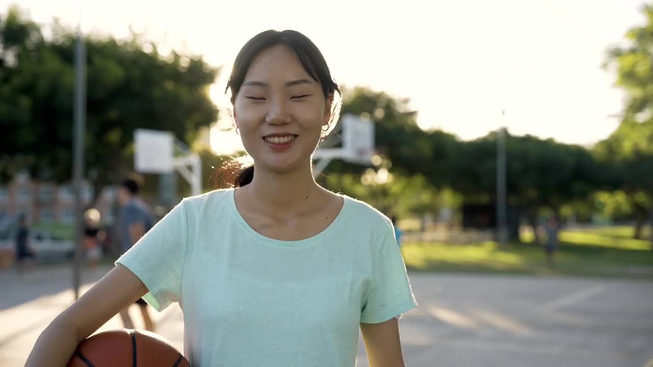 日落时分，年轻的亚洲女子在法庭上拿着篮球视频素材