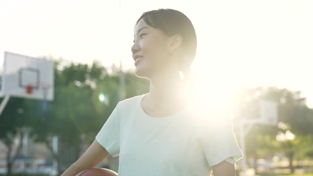 日落时分，年轻的亚洲女子在法庭上拿着篮球视频素材