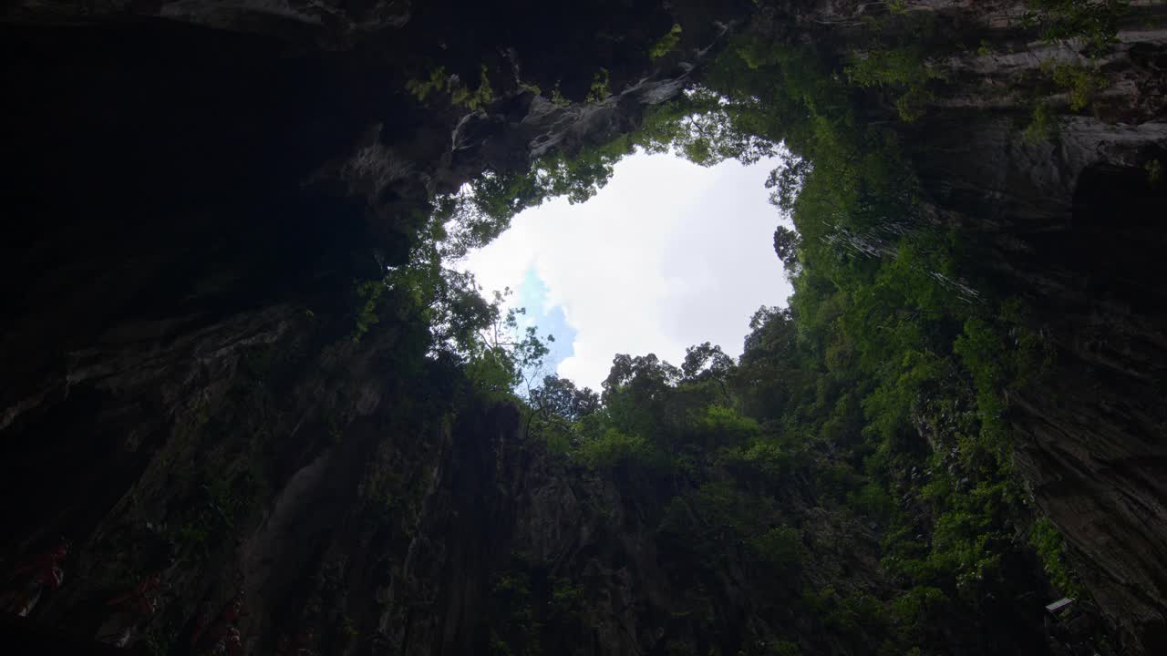 在吉隆坡的拔都洞，透过一个自然的开口看天空，周围是郁郁葱葱的绿色植物视频素材