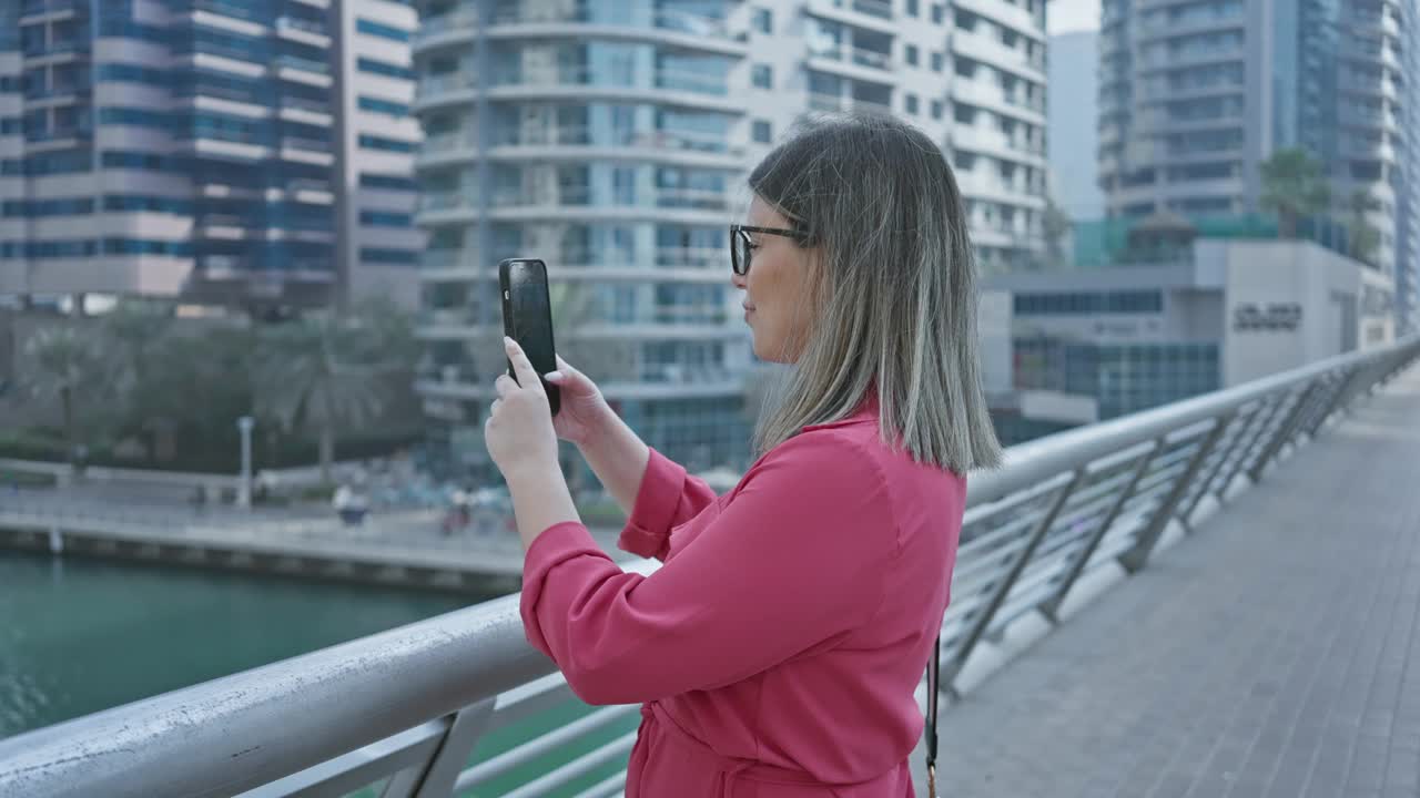 一名身穿粉色衬衫的女子用手机拍下了迪拜码头，展示了奢华、旅游和科技。视频素材