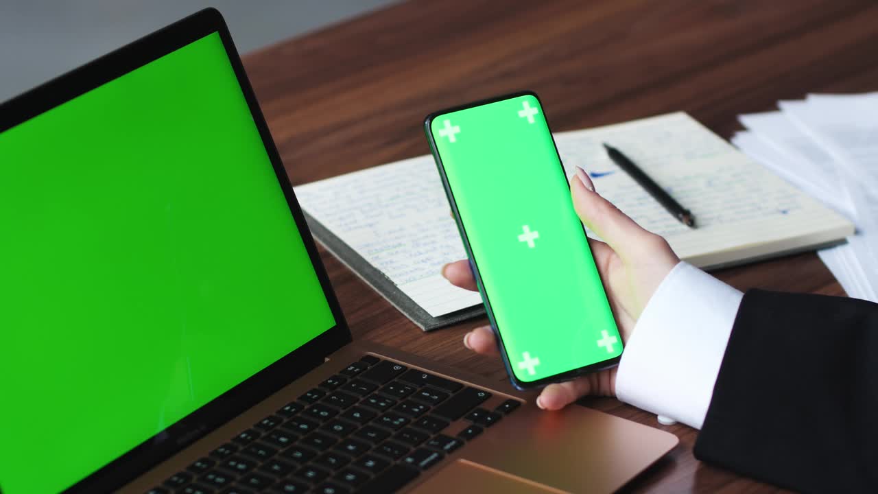 近距离使用智能手机绿屏和笔记本电脑Chromakey的女人。女人手持手机的特写镜头。色度键和绿屏的概念视频素材