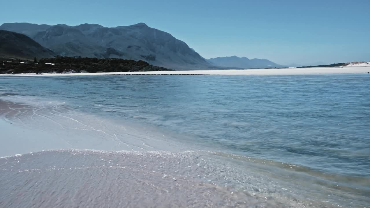 一个泻湖口流入海洋，海浪轻轻翻滚，在南非赫曼努斯山脉的远处视频素材