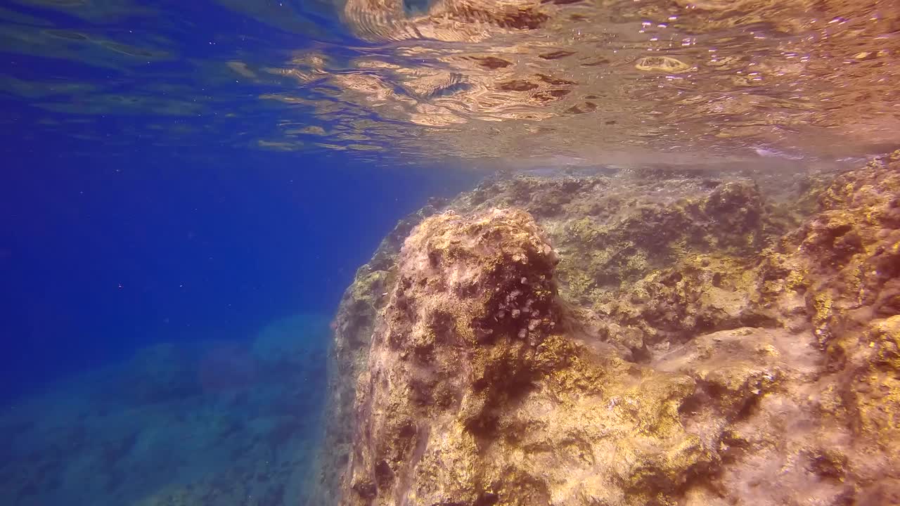 相机沿着陡峭的悬崖向前移动，反射在水面上，在蓝色的水背景视频素材