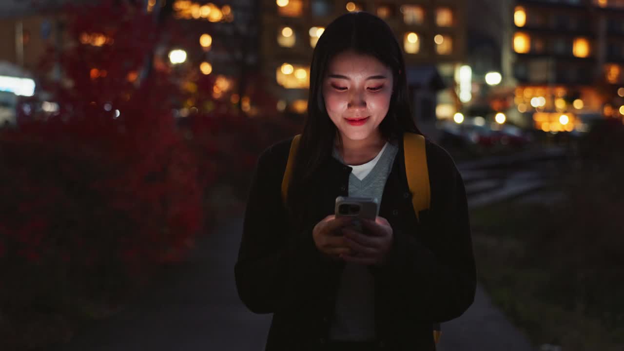 快乐的日本女人，在晚上打电话，在城市里散步，交流，社交媒体或户外网络。晚上在市区用手机上网聊天的女性视频素材