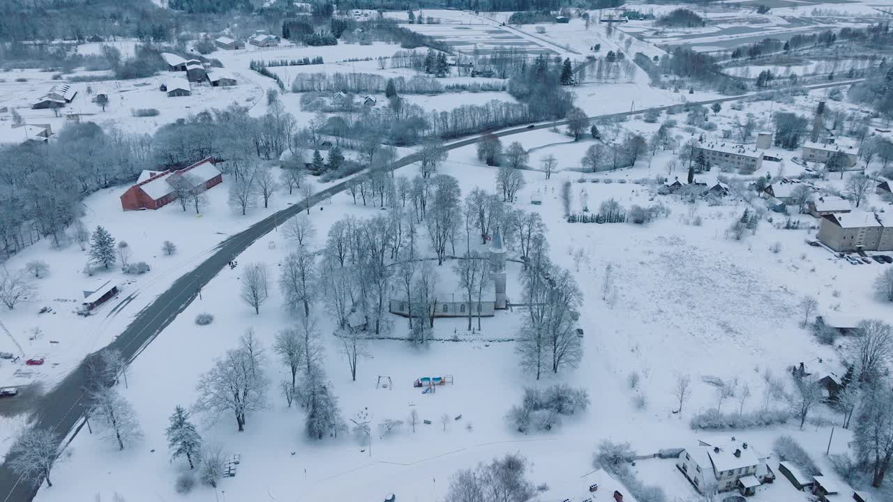 在Renda村(Kuldiga教区，拉脱维亚)，白雪覆盖的风景，道路和五颜六色的游乐场，冬天的风景，鸟瞰，向前移动，向下倾斜视频素材