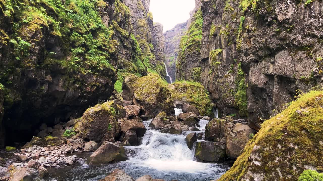 青苔覆盖的悬崖和冰岛峡谷的瀑布，多云的日光视频素材