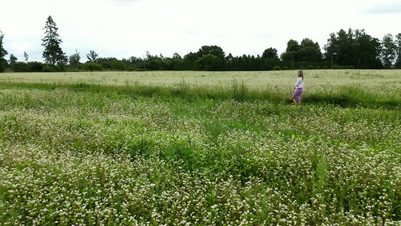 一个女人站在白色的花田里，周围是自然景观和天空视频素材