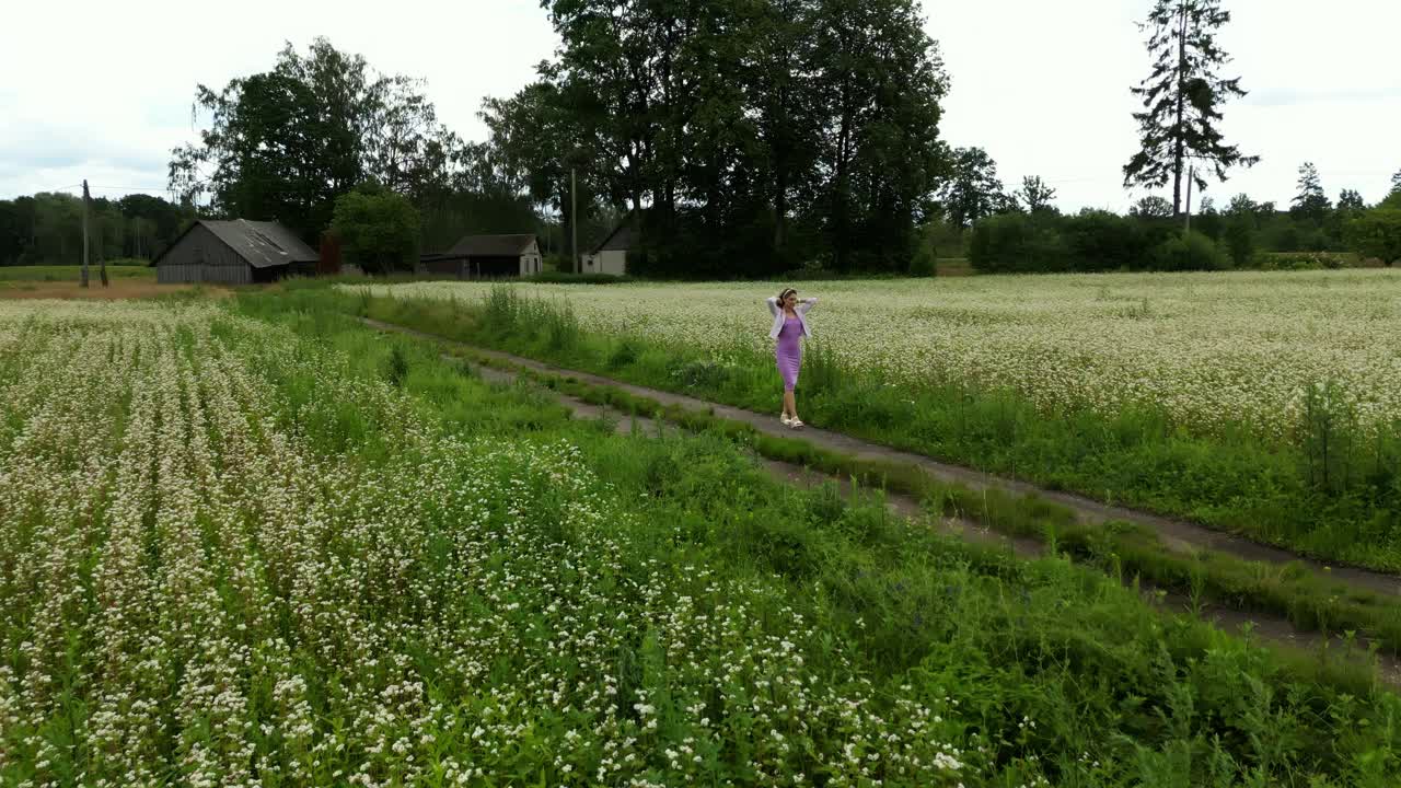 草地漫游癖:一个女人走在白色的花田里，被大自然和天空的美丽所包围视频素材