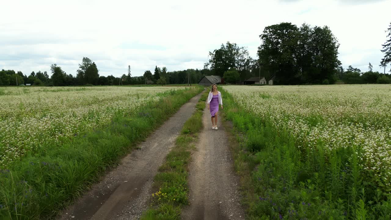 景观探索:女人漫步在白色的花田里，沉浸在广阔的自然环境和天空中视频素材