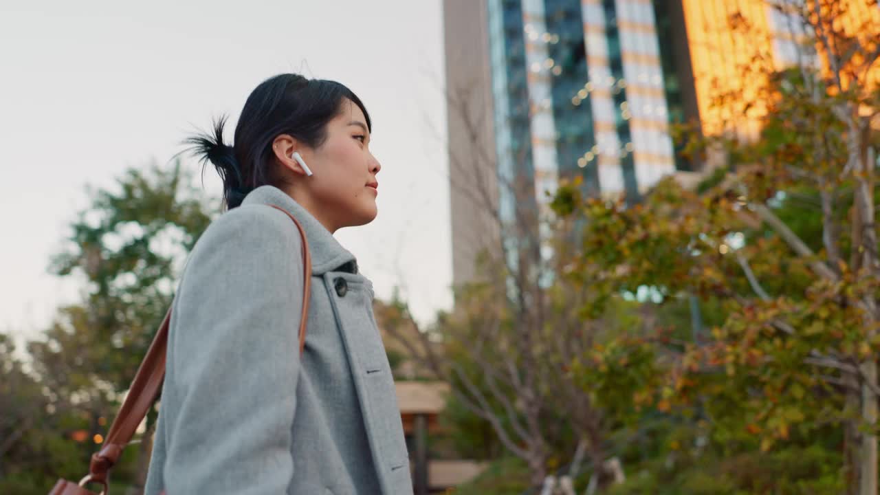 女性，亚洲和旅行，带着智能手机和耳机与城市里的专业人士一起上班。在旅途中听音乐，播客和通勤在东京的城市街道与播放列表视频素材