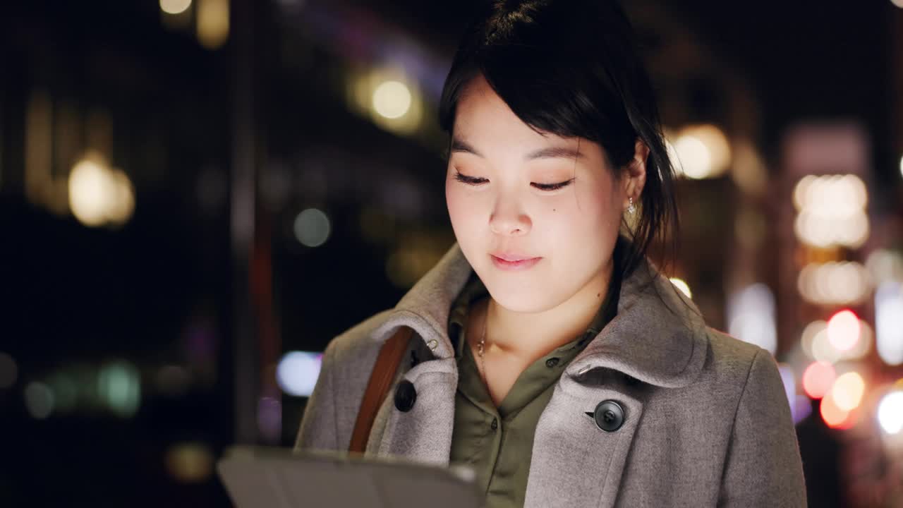 夜晚，城市，一个日本女人一边拿着平板电脑，一边想着gps定位、电子邮件或搜索。数字，想法和女孩在日本的黑暗中输入技术，同时在线阅读以获取灵感视频素材