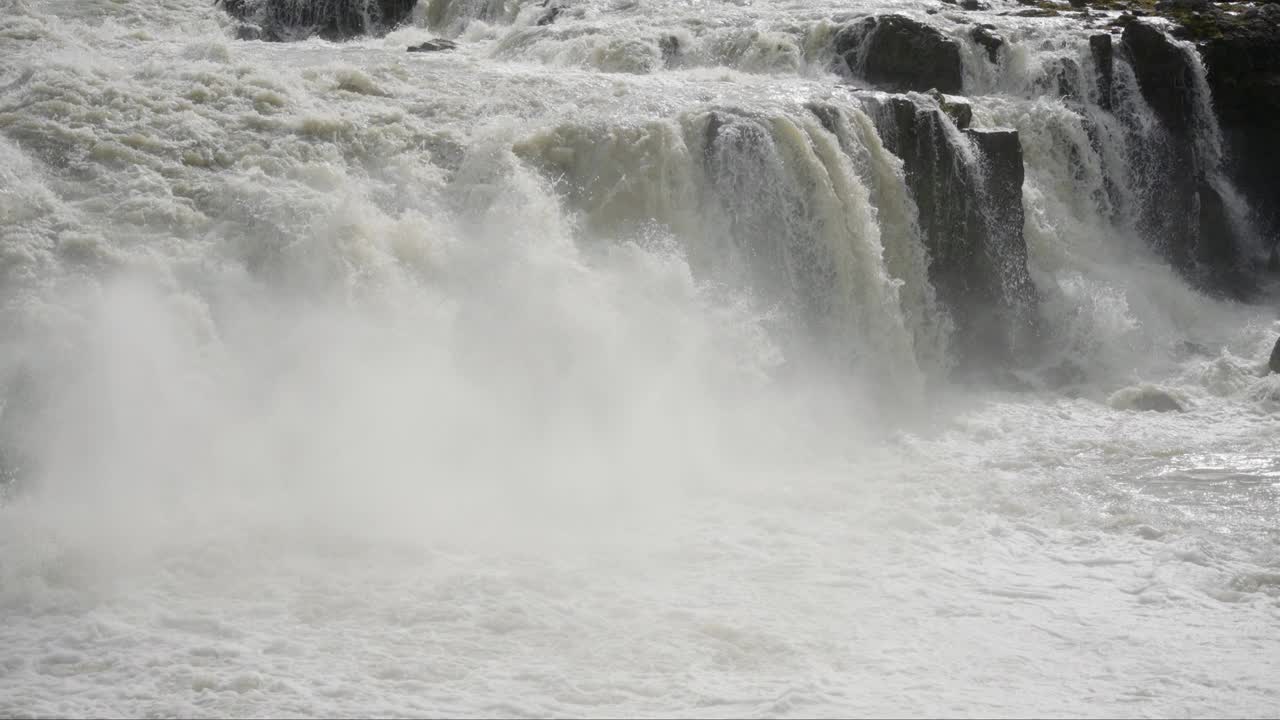 壮观的平移镜头，一系列巨大的瀑布倾泻入白色泡沫的河流。用辉煌的慢动作拍摄。视频素材