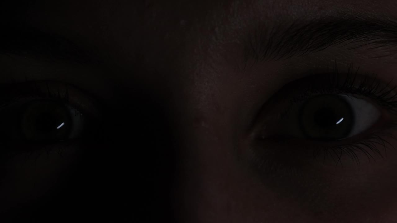 女孩睁大的眼睛在黑色背景上闪烁，特写视频素材