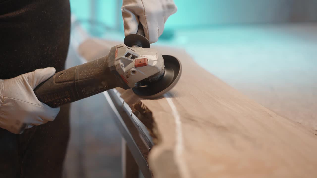 细木工在车间用角磨机打磨原木板，在打磨木材表面时飞木屑，在车间与原木板一起工作视频素材