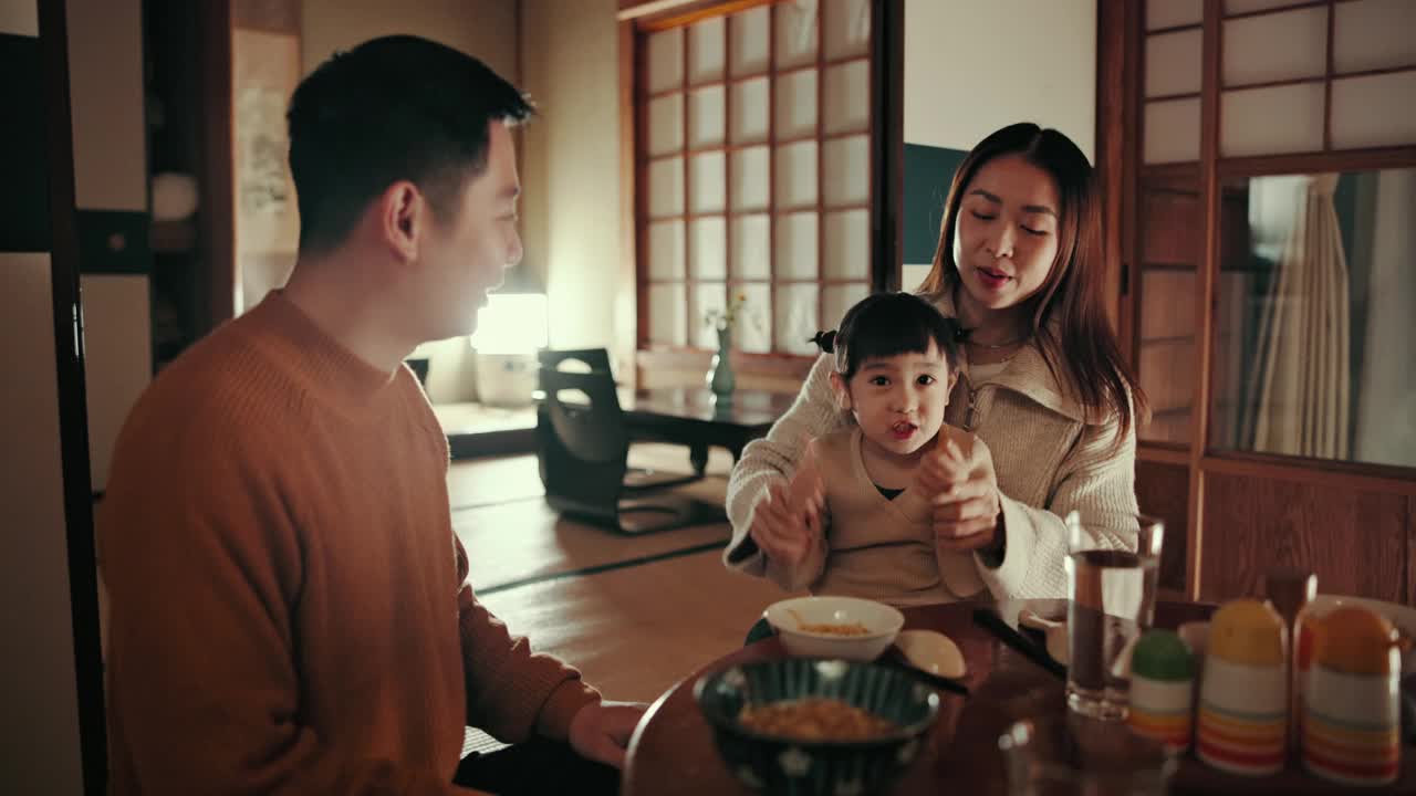 日本父母用鞠躬和女生吃饭，用面带微笑和教感恩，晚上在家和营养。孩子，妈妈和爸爸在东京的家庭住宅里吃食物，饮食和餐厅视频素材