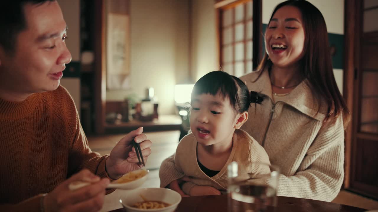 亚洲父母，孩子，在晚餐时微笑着喂养，帮助和照顾，在家里的夜晚或营养。在东京一所房子的餐厅里，孩子、母亲和父亲拿着食物、饮食和勺子视频素材