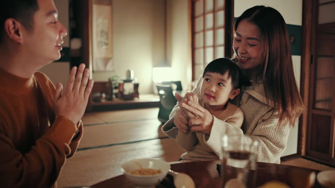 日本的父母，女孩和孩子用祈祷和晚餐，微笑和教感激用面条，晚上和营养在家里。孩子，妈妈和爸爸在东京的家庭住宅里寻找食物，信仰和餐厅视频素材