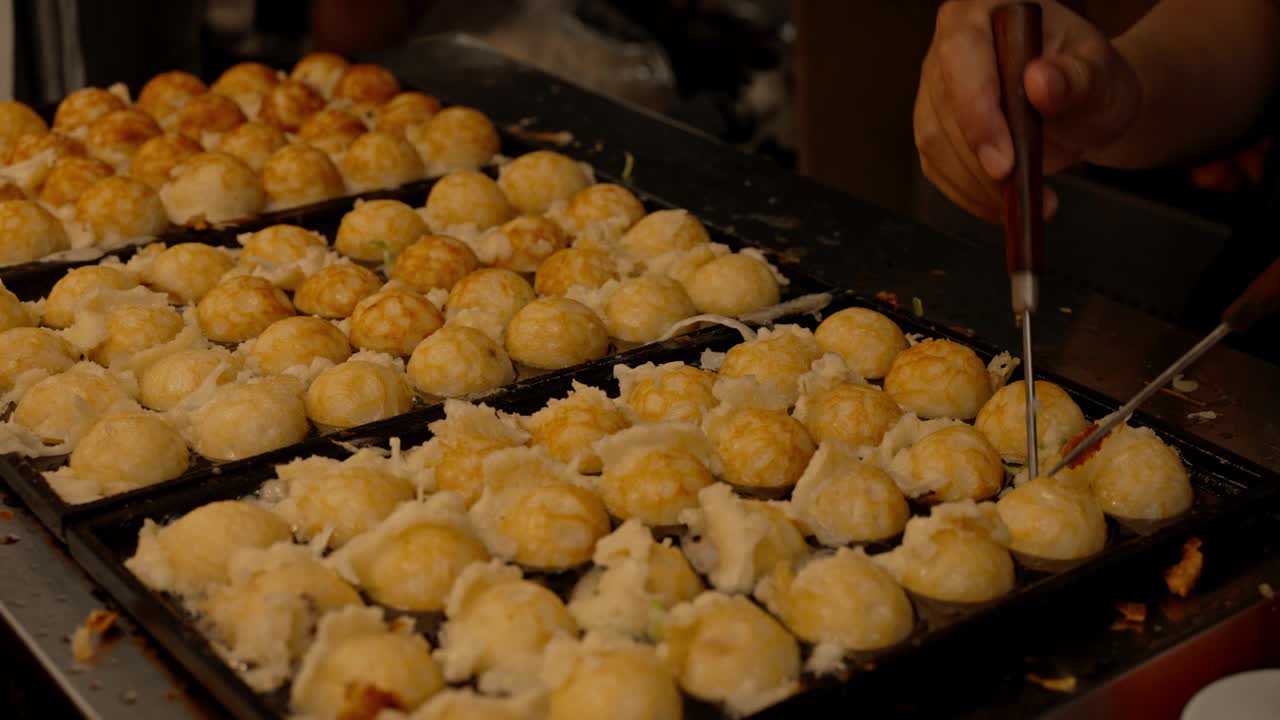 在街头食品市场，厨师用特制的铁锅手工制作日本传统的球形小吃章鱼烧。视频下载