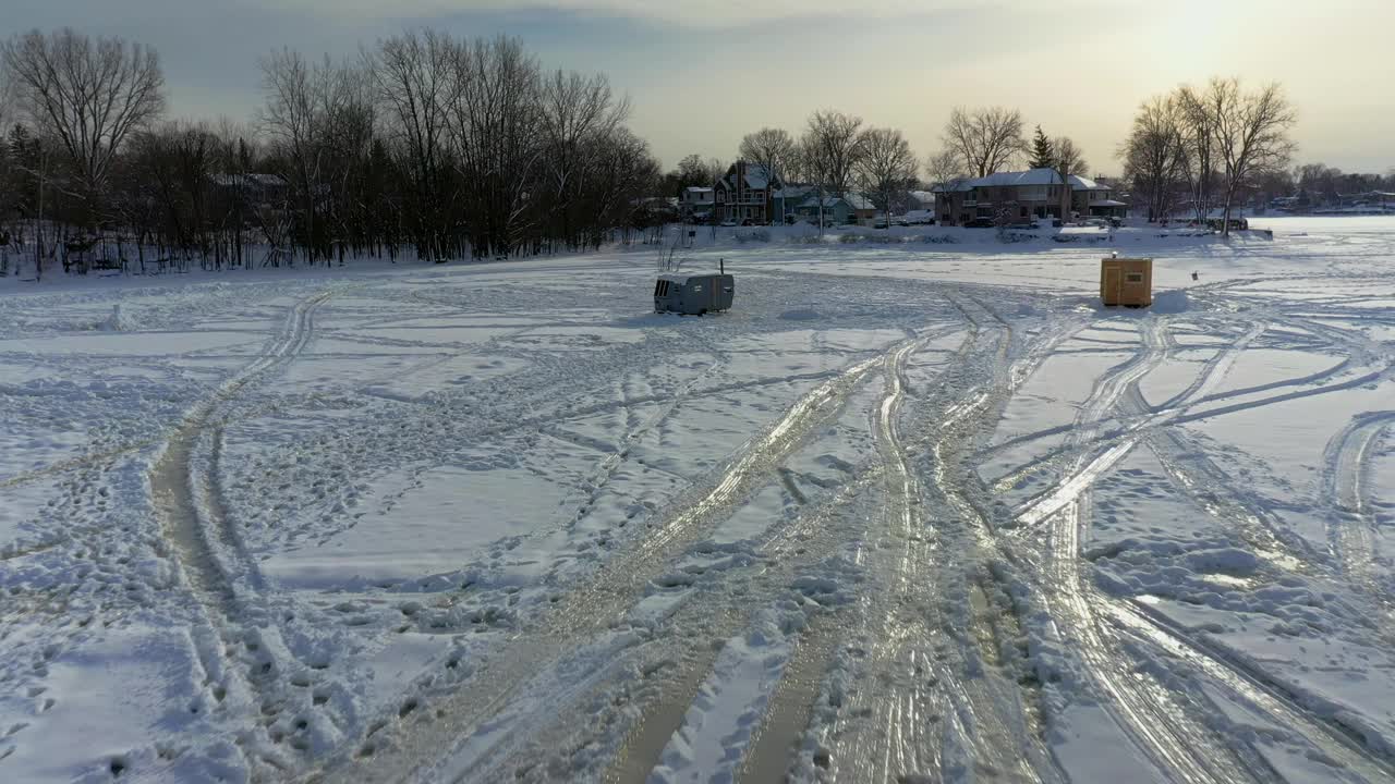 空中无人机视图向后移动在雪地上留下的轨道上，并在冰冻的冰上显示人们在日落时在拉瓦尔西部的白色雪地中行走-每秒24帧视频素材