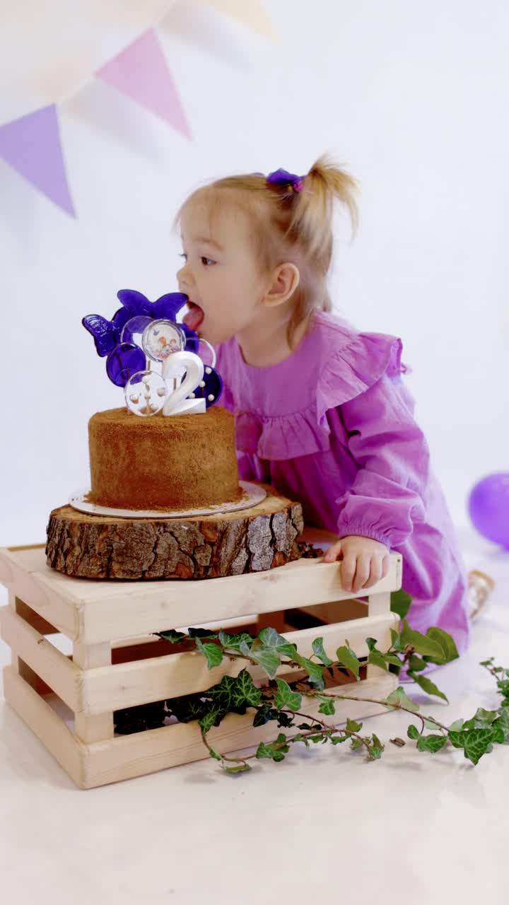 可爱的小女孩庆祝生日快乐，并在家里舔生日蛋糕上的棒棒糖视频素材