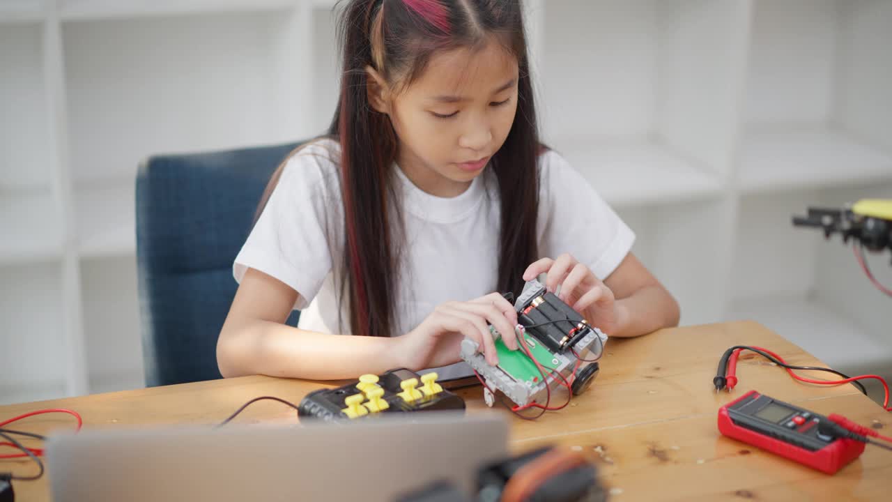 年轻的亚洲女孩在她的平板电脑的在线教程的帮助下学习组装汽车机器人视频素材