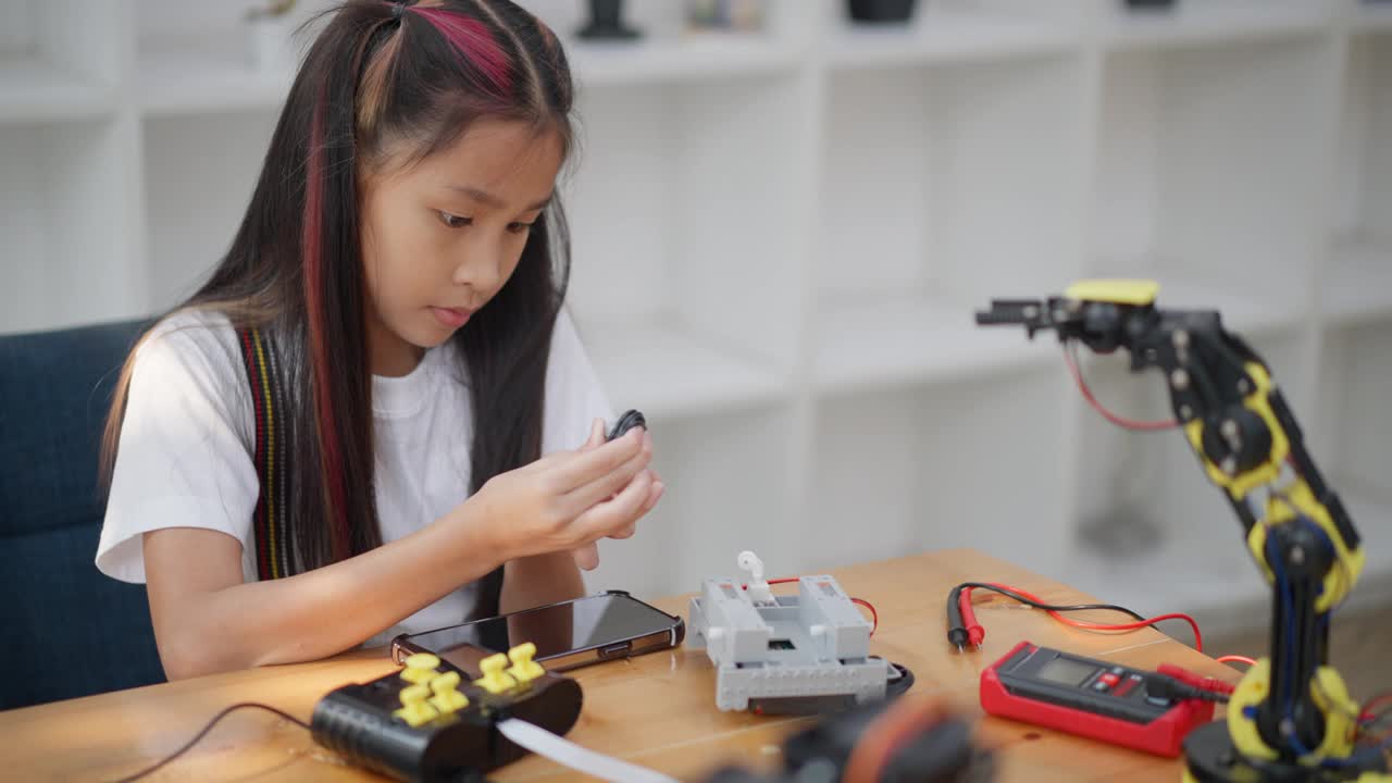 年轻的亚洲女孩在她的平板电脑的在线教程的帮助下学习组装汽车机器人视频素材