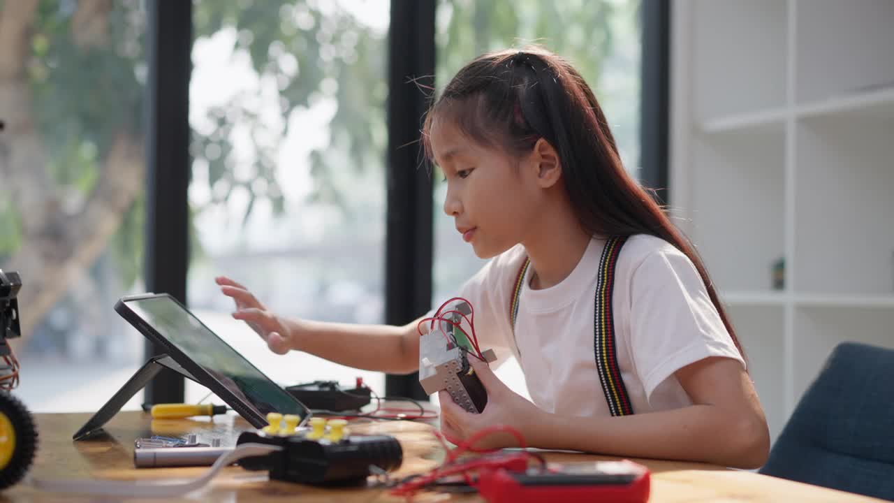 年轻的亚洲女孩在她的平板电脑的在线教程的帮助下学习组装汽车机器人视频素材