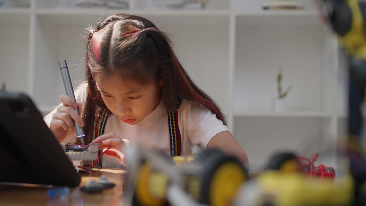 年轻的亚洲女孩在她的平板电脑的在线教程的帮助下学习组装汽车机器人视频素材