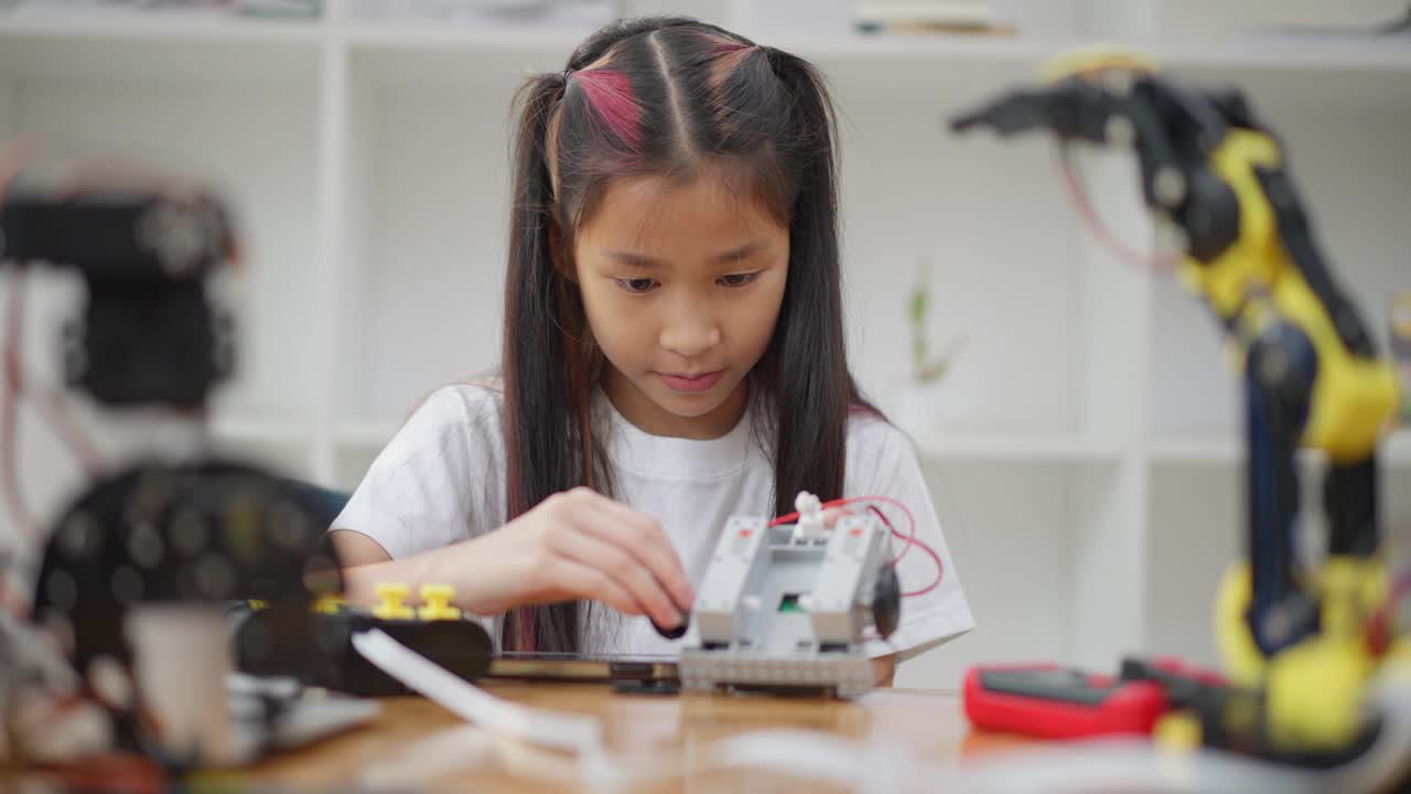 年轻的亚洲女孩在她的平板电脑的在线教程的帮助下学习组装汽车机器人视频素材