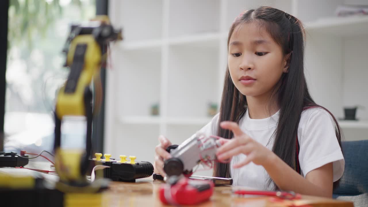 年轻的亚洲女孩在她的平板电脑的在线教程的帮助下学习组装汽车机器人视频素材