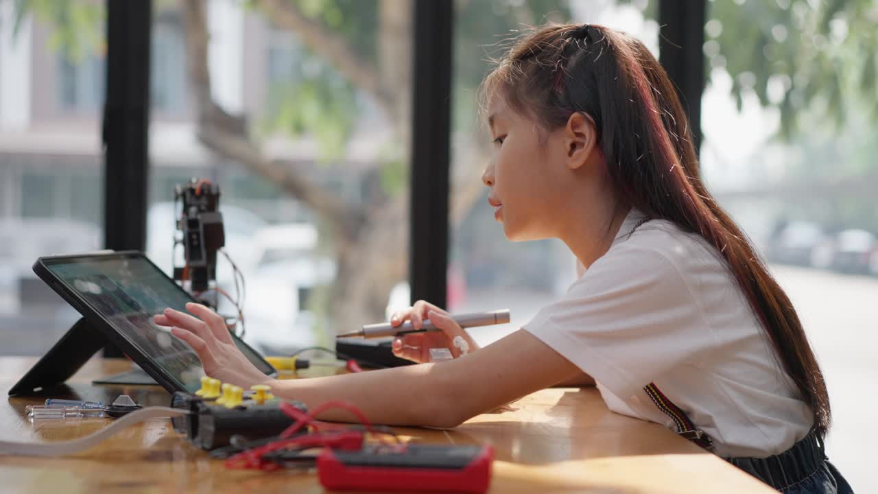 年轻的亚洲女孩在她的平板电脑的在线教程的帮助下学习组装汽车机器人视频素材