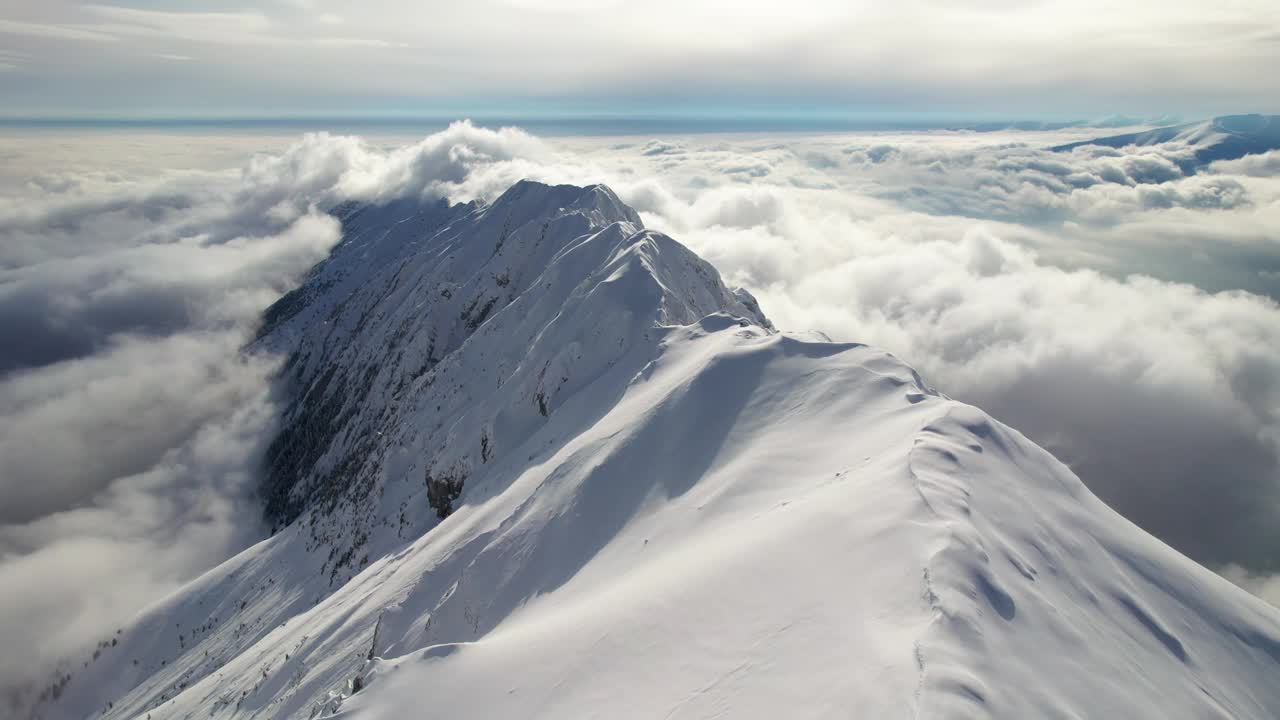 白雪覆盖的Piatra Craiului山脉在蓝天下的云海中达到顶峰，鸟瞰图视频素材