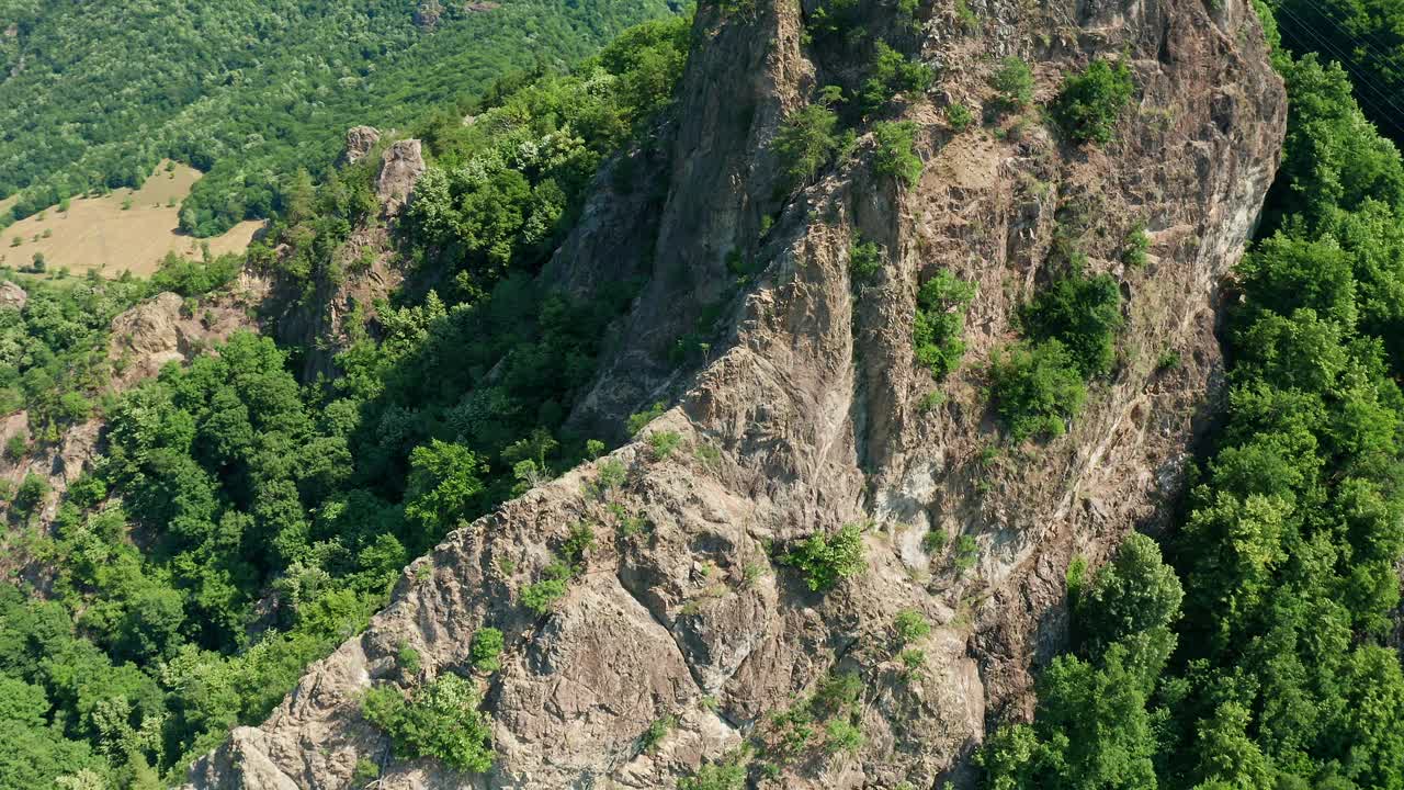 在晴朗的天空下，郁郁葱葱的绿叶覆盖了崎岖的Pietrele Rosiei峰，鸟瞰图视频素材