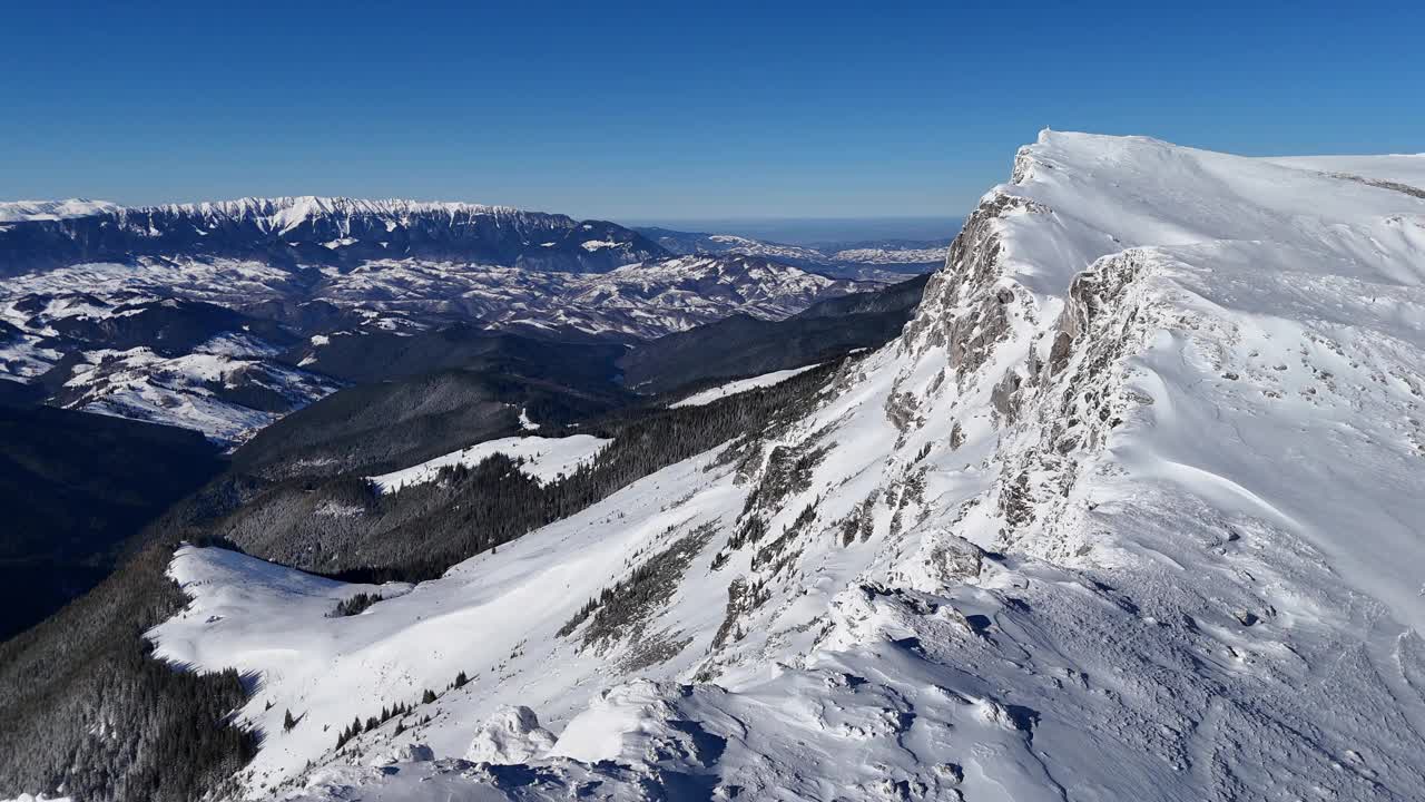 白雪皑皑的Piatra Craiului山峰在晴朗的蓝天下从buegi山脉鸟瞰视频素材