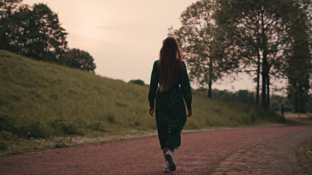 年轻美丽的女人在夏日的大自然中穿着绿色的长裙散步。视频素材