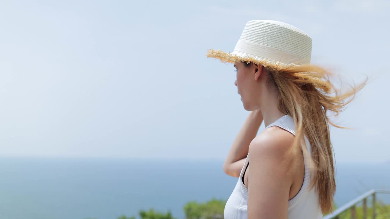 一位戴着遮阳帽的孤独女游客站在那里看着美丽的大海。视频素材