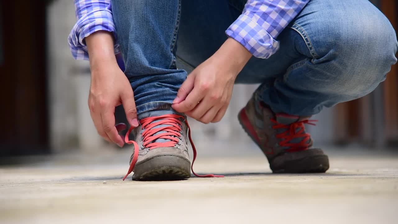 绿色自然人跪在公园的绿草地上系鞋带。近距离拍摄的男子双手系鞋带为他的施工棕色靴子。近距离男子双手绑鞋为鞋履概念。视频素材