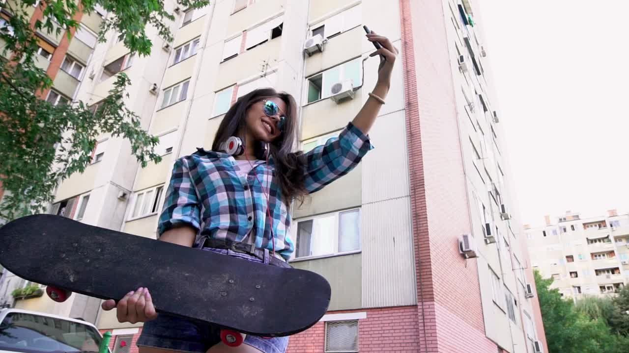 年轻的时髦女人拿着滑板在街上自拍视频素材