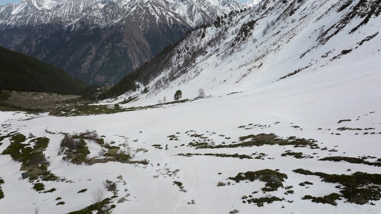 鸟瞰运动员滑雪自由骑在山坡上野外极限运动休闲冬季景观。一名男子在春季自由骑行时的残雪上放松视频素材