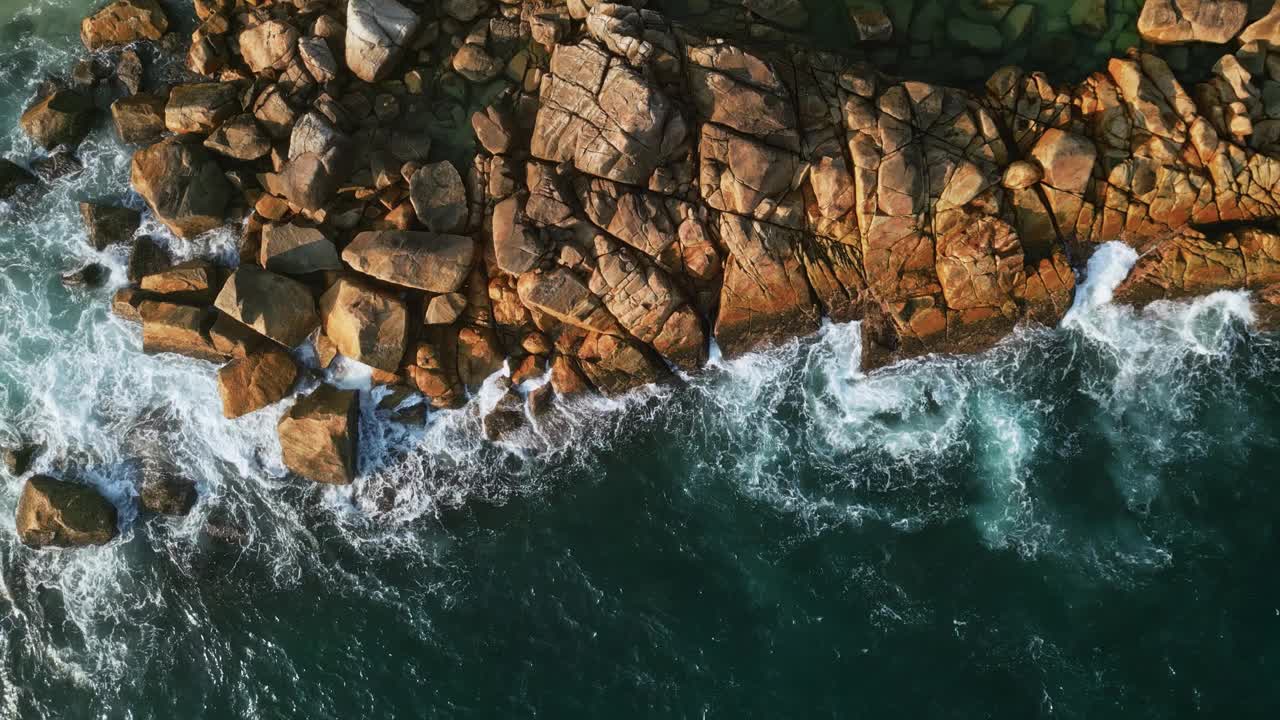 空中生动的蓝色海浪冲击着热带海岸线。鸟瞰动态的水运动，图案由泡沫，深海蓝色沿岩石。从上面向下看。慢动作视频素材