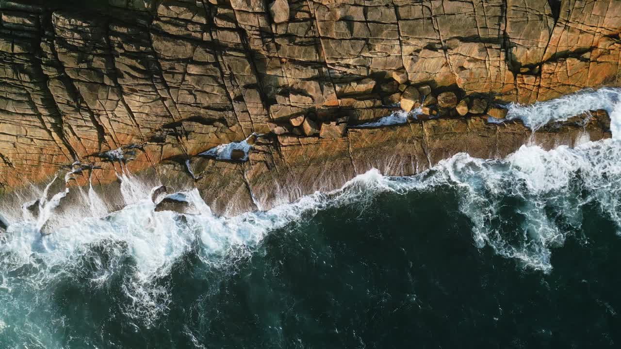 鸟瞰图海浪冲击着热带岩石海岸，原始的蓝色海洋与崎岖的海岸线相遇。无人机强大的海浪打碎石头产生泡沫，自然美景旅游，生态纪录片，自然电影。视频素材