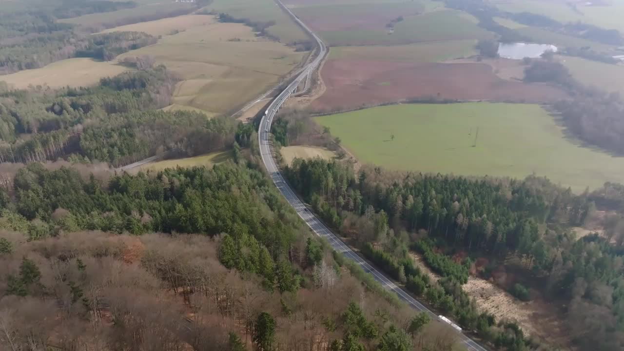 道路上有过往的汽车和卡车。在农村环境中建立的用于运送货物和运送人员的基础设施。到处都是森林和田野。鸟瞰图视频素材