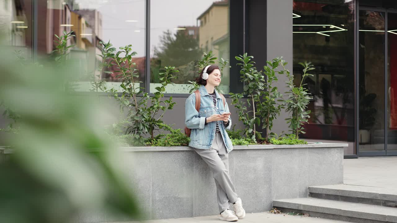 一位戴着耳机的年轻女学生正在户外听音乐视频素材