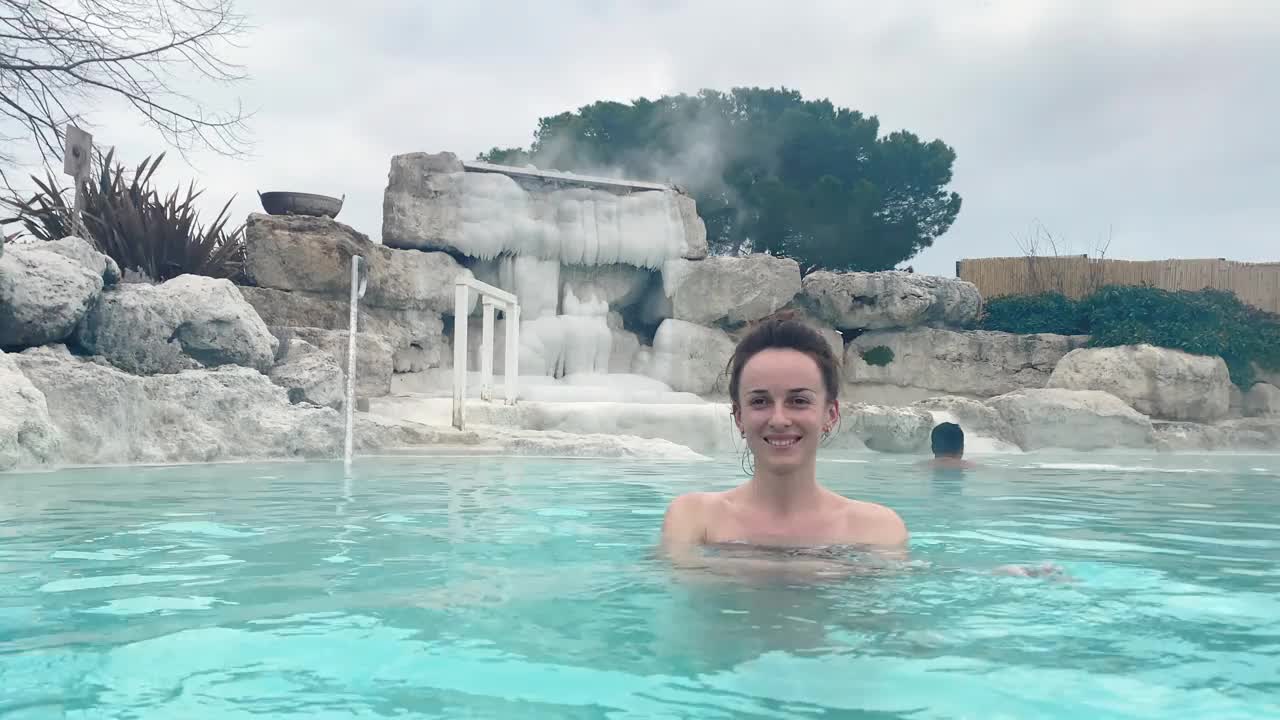 在露天的热水池里微笑的女人，在天然地热浴池里放松一天，底部有硫磺泥和治疗蒸汽，治疗免疫系统和健康视频下载