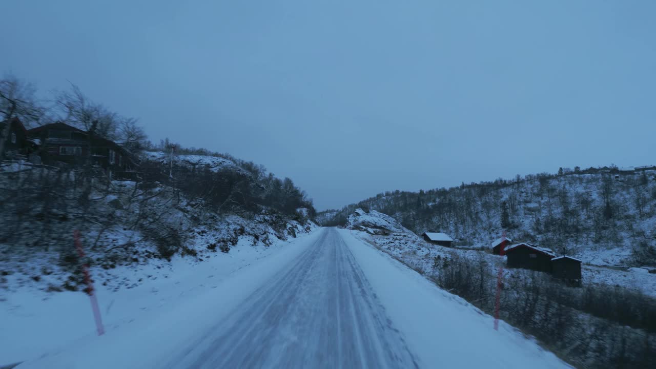 挪威被雪覆盖的道路上，无人机在暮色中向一辆汽车快速移动视频素材