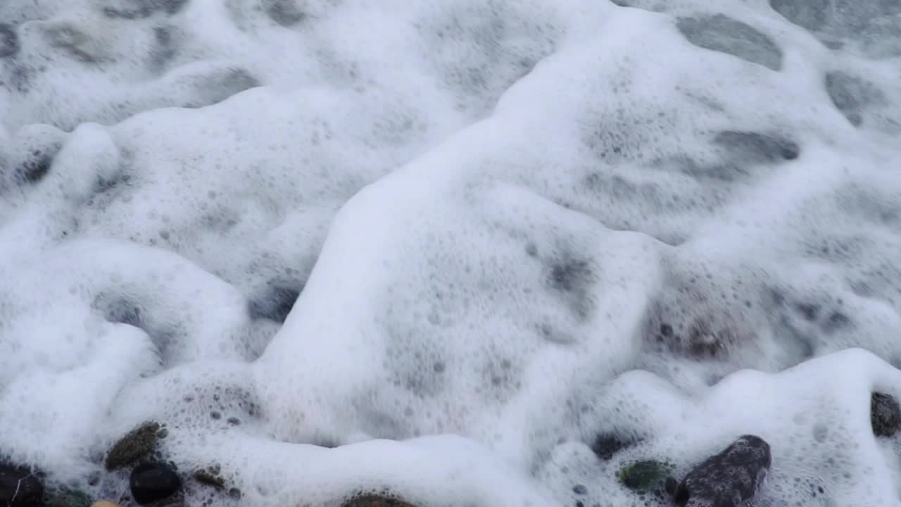 汹涌的海浪拍打着卵石海岸线，展示着海洋的美丽和力量。视频素材