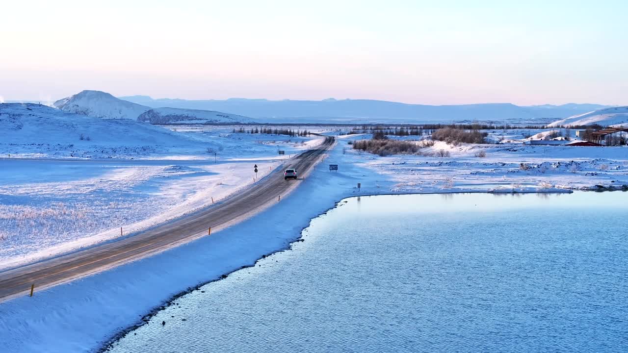 冬天的道路蜿蜒穿过白雪皑皑的米瓦恩火山景观，黄昏时分，湖面平静，光线柔和视频素材